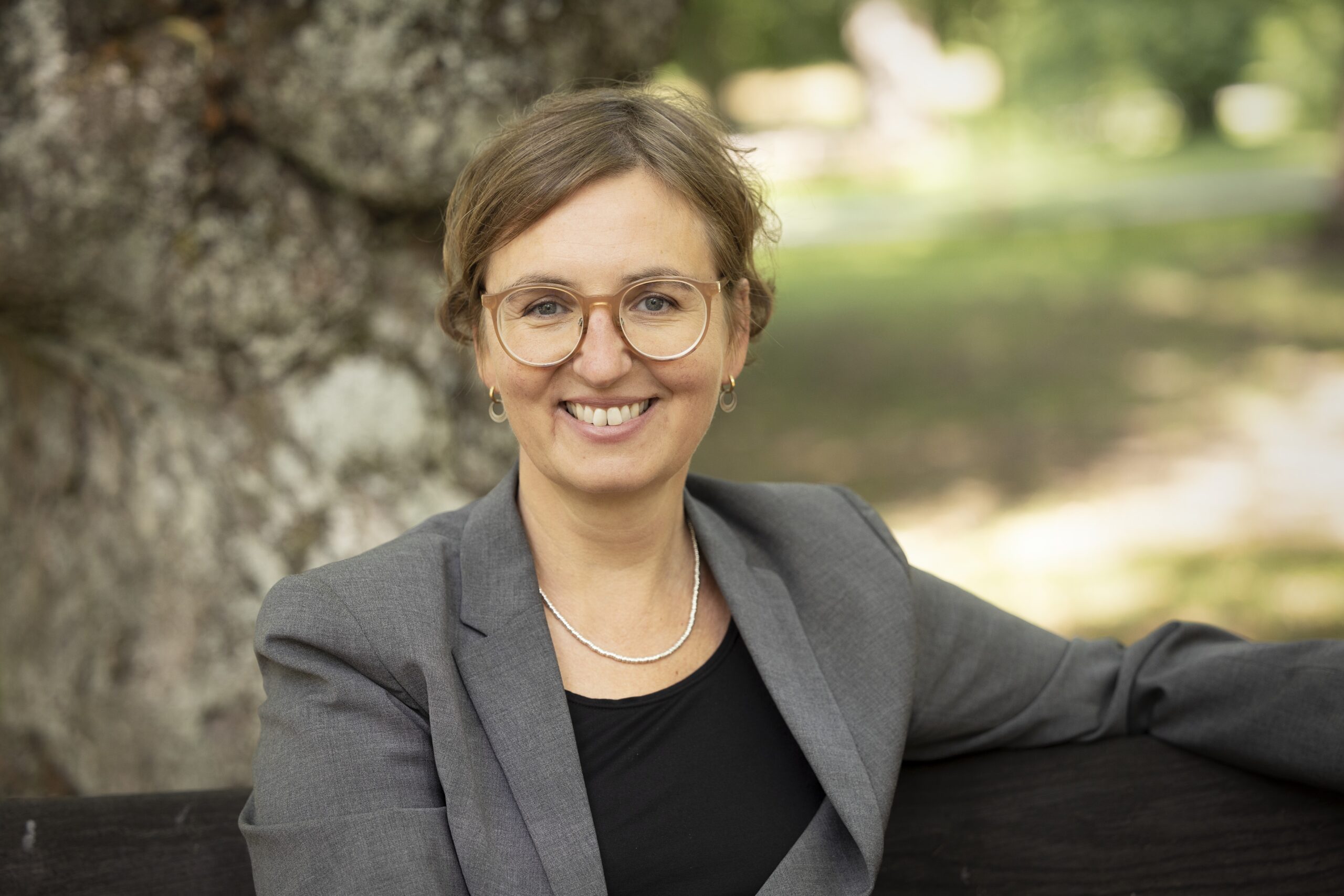 Prof. Emily A. Holmes sitting on a park bench and smiling.